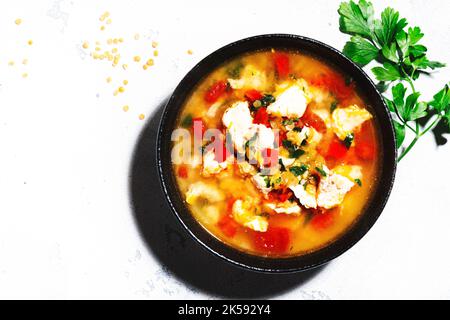 Wärmende Herbstsuppe mit roten Linsen, Hühnerfilet, Gemüse, Gewürzen und Paprika, Gemüsefutter. Weißer Tisch, hartes Licht, Draufsicht Stockfoto