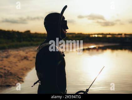 Seitenansicht eines männlichen Tauchers, der Neoprenanzug und Schnorchelausrüstung am Meer trägt. Speer Fischer Blick in das Meer, während eine Speergun halten. Stockfoto