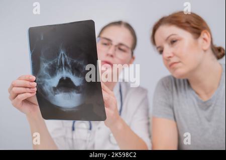 Eine Ärztin und ein Patient an der Rezeption diskutieren über eine Röntgenaufnahme der Nebenhöhlen. Stockfoto