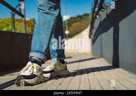 Nahaufnahme der Beine einer Frau, die in Jeans und Turnschuhen die Straße entlang geht. Konzept des weiblichen, gesunden Lebens, Mode. Copyspace. Stockfoto