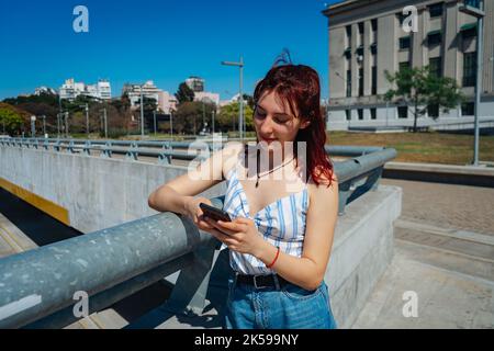 Junge Rotschopf-Frau, die Nachrichten auf ihrem Handy überprüft, zufriedene Haltung. Speicherplatz kopieren. Ausrichtung im Querformat. Stockfoto