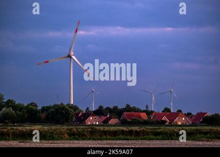 29.08.2022, Deutschland, Niedersachsen, Jemgum - Wohngebäude, dahinter Windturbinen. Jemgum ist ein Kavernenlager, in dem Hohlräume sind Stockfoto