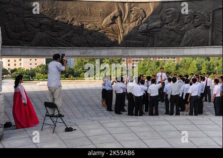 08.08.2012, Nordkorea, Pjoengjang - Eine Gruppe nordkoreanischer Studenten steht unter einem riesigen Bronzerelief am Denkmal zur Gründung des Arbeiters Stockfoto