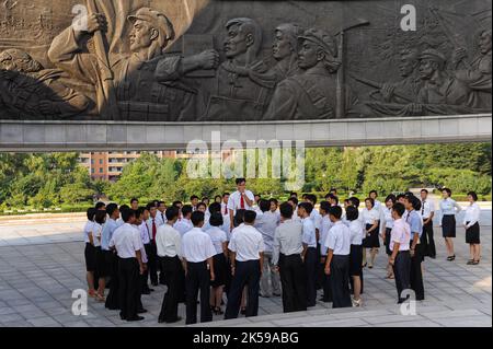 08.08.2012, Nordkorea, Pjoengjang - Eine Gruppe nordkoreanischer Studenten steht unter einem riesigen Bronzerelief am Denkmal zur Gründung des Arbeiters Stockfoto