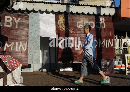 16.12.2013, Myanmar, Yangon - eine alltägliche Szene zeigt einen Mann in einem traditionellen Umhüllenrock (longyi) auf dem Fußweg neben einer Straße vor dem SM Stockfoto