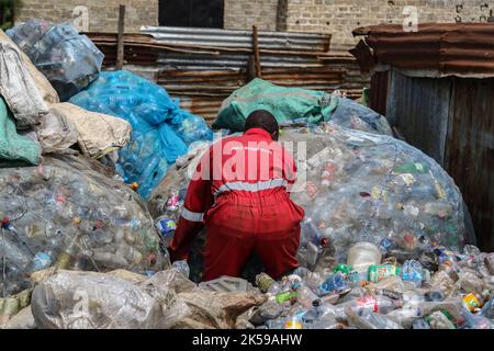 Kisumu, Nyanza, Kenia. 4. Oktober 2022. Ein Mann, der eine Coca-Coca-Firma mit rotem Overall trägt, der mit der Aufschrift „Welt ohne Abfall“ bestickt ist, wird in einem Abfallsammelzentrum für Plastikmüll in Kisumu arbeiten sehen. Aktivisten und Umweltgruppen in Kenia und anderen Teilen der Welt haben die Coca-Cola Company als Sponsor des diesjährigen Klimagipfels COP 27, der im November in Ägypten stattfinden wird, verächtet. (Bild: © James Wakibia/SOPA Images via ZUMA Press Wire) Stockfoto