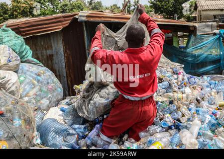 Kisumu, Nyanza, Kenia. 4. Oktober 2022. Ein Mann, der eine Coca-Coca-Firma mit rotem Overall trägt, der mit der Aufschrift „Welt ohne Abfall“ bestickt ist, wird in einem Abfallsammelzentrum für Plastikmüll in Kisumu arbeiten sehen. Aktivisten und Umweltgruppen in Kenia und anderen Teilen der Welt haben die Coca-Cola Company als Sponsor des diesjährigen Klimagipfels COP 27, der im November in Ägypten stattfinden wird, verächtet. (Bild: © James Wakibia/SOPA Images via ZUMA Press Wire) Stockfoto