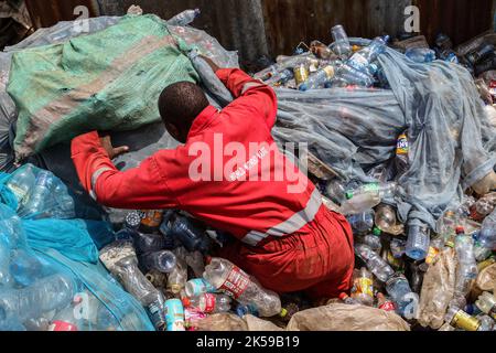 Kisumu, Nyanza, Kenia. 4. Oktober 2022. Ein Mann, der eine Coca-Coca-Firma mit rotem Overall trägt, der mit der Aufschrift „Welt ohne Abfall“ bestickt ist, wird in einem Abfallsammelzentrum für Plastikmüll in Kisumu arbeiten sehen. Aktivisten und Umweltgruppen in Kenia und anderen Teilen der Welt haben die Coca-Cola Company als Sponsor des diesjährigen Klimagipfels COP 27, der im November in Ägypten stattfinden wird, verächtet. (Bild: © James Wakibia/SOPA Images via ZUMA Press Wire) Stockfoto