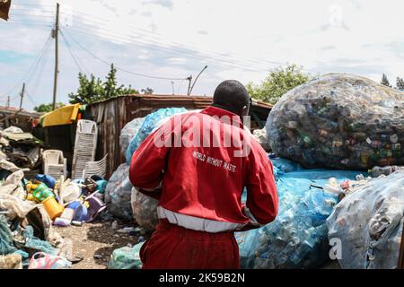 Kisumu, Nyanza, Kenia. 4. Oktober 2022. Ein Mann, der eine Coca-Coca-Firma mit rotem Overall trägt, der mit der Aufschrift „Welt ohne Abfall“ bestickt ist, wird in einem Abfallsammelzentrum für Plastikmüll in Kisumu arbeiten sehen. Aktivisten und Umweltgruppen in Kenia und anderen Teilen der Welt haben die Coca-Cola Company als Sponsor des diesjährigen Klimagipfels COP 27, der im November in Ägypten stattfinden wird, verächtet. (Bild: © James Wakibia/SOPA Images via ZUMA Press Wire) Stockfoto