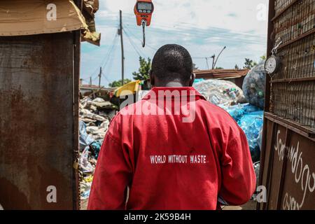 Kisumu, Nyanza, Kenia. 4. Oktober 2022. Ein Mann, der eine Coca-Coca-Firma mit rotem Overall trägt, der mit der Aufschrift „Welt ohne Abfall“ bestickt ist, wird in einem Abfallsammelzentrum für Plastikmüll in Kisumu arbeiten sehen. Aktivisten und Umweltgruppen in Kenia und anderen Teilen der Welt haben die Coca-Cola Company als Sponsor des diesjährigen Klimagipfels COP 27, der im November in Ägypten stattfinden wird, verächtet. (Bild: © James Wakibia/SOPA Images via ZUMA Press Wire) Stockfoto