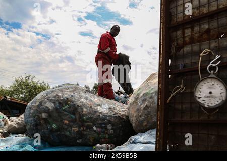 Kisumu, Nyanza, Kenia. 4. Oktober 2022. Ein Mann, der eine Coca-Coca-Firma trägt, in einem roten Overall, der mit der Aufschrift ''Welt ohne Abfall'' bestickt ist, steht auf einem Haufen Plastikflaschen in einem Plastikmüllsammelzentrum in Kisumu. Aktivisten und Umweltgruppen in Kenia und anderen Teilen der Welt haben die Coca-Cola Company als Sponsor des diesjährigen Klimagipfels COP 27, der im November in Ägypten stattfinden wird, verächtet. (Bild: © James Wakibia/SOPA Images via ZUMA Press Wire) Stockfoto