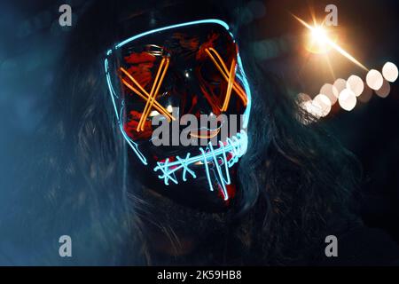 Mann mit langen zerlausenden Haaren in einer leuchtenden neonleuchtenden Maske. Stockfoto