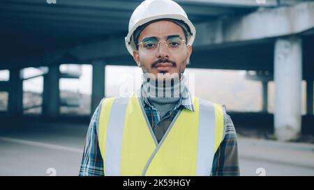 Porträt eines jungen arabischen Mannes in Uniform, der allein in der Industriezone steht und die Kamera anschaut. Beschäftigung und Professionals Konzept. Stockfoto
