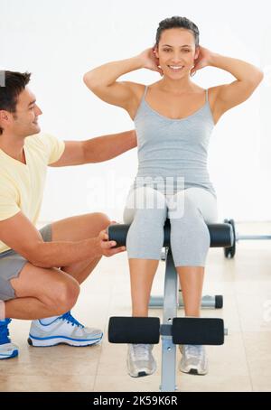 Helfen Sie ihr dabei, richtig zu trainieren. Ein Fitnesstrainer, der einer jungen Frau zeigt, wie sie eine Übung macht. Stockfoto