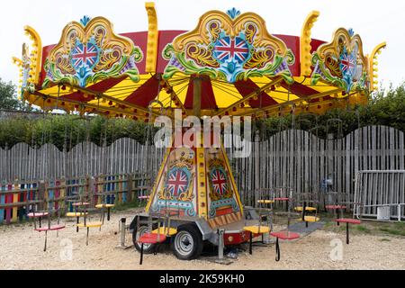 Leeres, farbenfrohes mobiles Karussell mit Stühlen, die an einer Kette hängen, reich verziert mit Bildern englischer Flaggen irgendwo in einem Dorf in Großbritannien Stockfoto