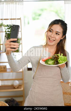 Portrait, schöne und gesunde junge asiatische Frau, die Selfie von sich selbst und ihrem hausgemachten Salat macht. Gesundes Lifestyle-Konzept Stockfoto