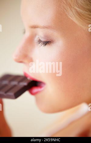 MMM, was für ein erstaunlicher Geschmack. Junge Frau genießt ein köstliches Stück Schokolade - Seitenansicht. Stockfoto