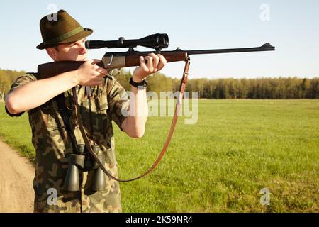 Auf den richtigen Schuss zielen. Ein Wildjäger, der mit seinem Scharfschützengewehr im Freien in der Tierwelt unterwegs ist. Stockfoto