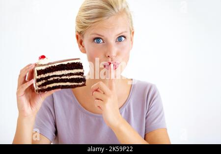 Shh, sagen Sie niemandem - Diäten. Junge Frau mit einem Stück Schokoladenkuchen und gestikulierenden Geheimnissen. Stockfoto