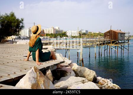 Tourist Frau sitzt am Meer entspannt mit trabucco traditionelle Fischmaschine in Termoli Dorf, Molise, Italien Stockfoto