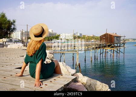 Urlaub Italy im Sommer. Rückansicht einer jungen Frau, die am Meer saß, entspannt mit der alten Trabucco-Fischmaschine an der Adria, Italien. Stockfoto