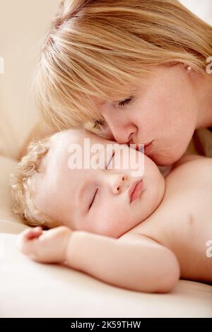 Sie kann nicht widerstehen, ihm einen Kuss zu geben. Kleiner Junge, der schlafend liegt, als seine Mutter ihn küsst. Stockfoto