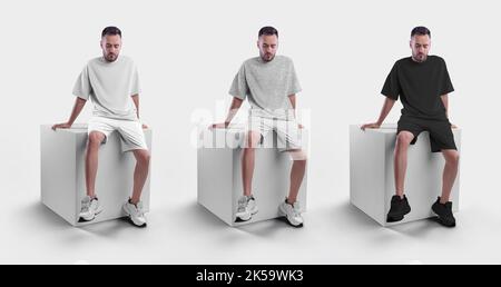 Modell aus weißem, schwarzem und grauem Herren-T-Shirt mit Shorts auf einem Mann, der auf einem Würfel sitzt. Bekleidungsvorlage für Präsentationen von Design, Druck, Stockfoto