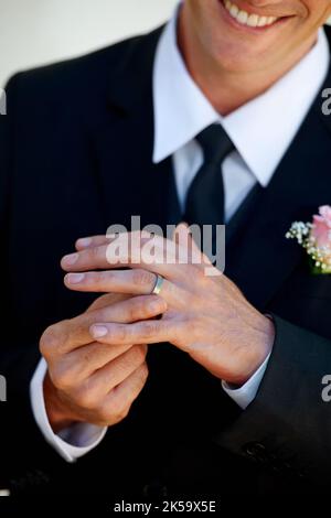Glücklich engagiert. Zugeschnittenes Bild eines glücklichen Bräutigams, der mit seinem Ehering spielt. Stockfoto