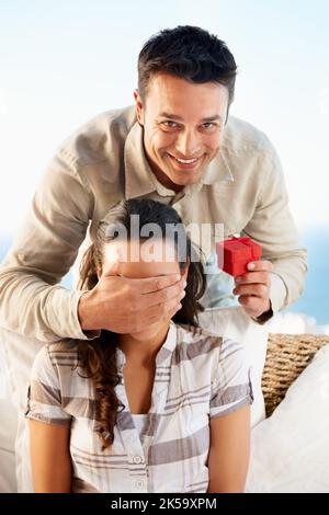 Sie hat keine Ahnung, was kommt. Ein junger Mann, der eine Ringbox mit der Hand auf die Augen seiner Freundinnen hält. Stockfoto