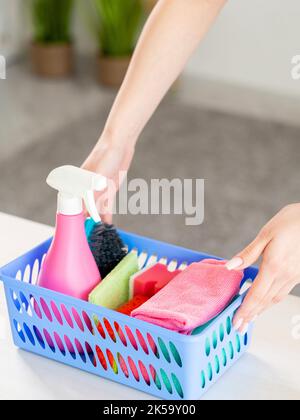 Hausarbeiten. Reinigungstag. Hausfrau arbeitet. Unkenntlich Frau Putting Korb mit Reiniger Spray Seifenschwämme Bürste Mikrofaser Tuch auf Tischleuchte Stockfoto