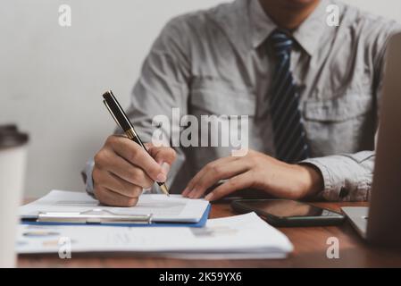 Hand halten Stift Schreiben Papierkram Geschäftsdokument finanzielle Investition oder Unterschrift Vertrag Job und Versicherung auf dem Schreibtisch. Stockfoto