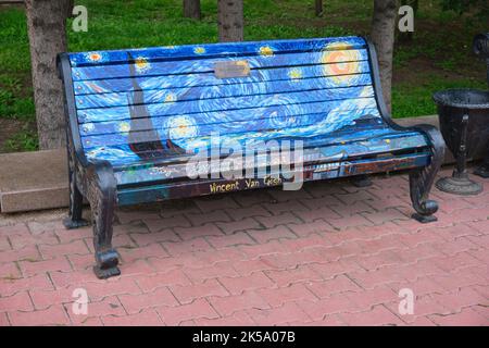 Eine klassische Holzlatte und eine Parkbank aus Metall mit einem Gemälde, das Vincent Van Goghs berühmtes Meisterwerk, die Sternennacht, nachbildet. In Astana, Nursultan, Kasachisch Stockfoto