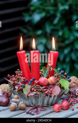 Herbstarrangement mit roten Kerzen, Hagebutten und Krabbenäpfeln in alter Backform Stockfoto