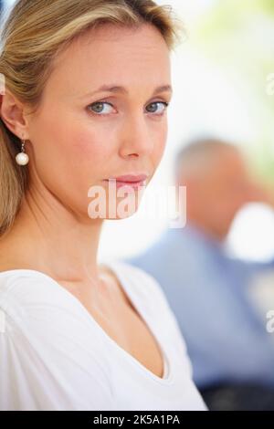 Ich bin mir nicht sicher, ob sie bleiben oder gehen soll... - Eheprobleme. Ernsthafte reife Frau, die mit ihrem Mann im Hintergrund besorgt aussieht. Stockfoto