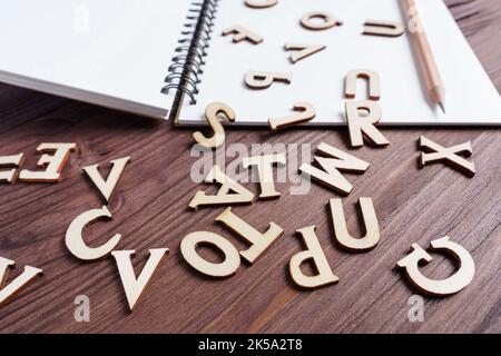 Notizbuch, Bleistift und Holzbuchstaben auf einem dunklen Holztisch verstreut. Stockfoto