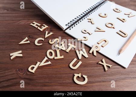 Schreibfertigkeiten beherrschen: Spiralnotizbuch, Bleistift und Holzbuchstaben auf einem dunklen Holztisch verstreut. Stockfoto