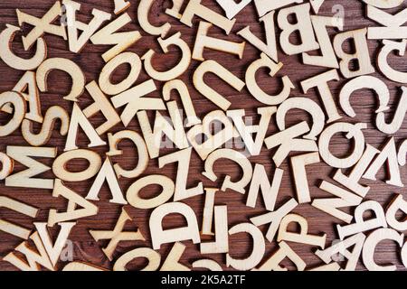 Abstrakter Hintergrund aus verstreuten Holzbuchstaben auf einem dunklen Holztisch. Stockfoto