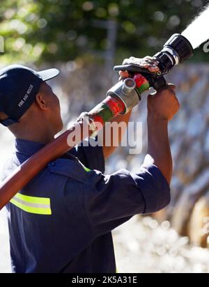 In einem Notfall kompetent. Rückansicht eines Feuerwehrmans, der Wasser mit einem Löschschlauch spritzt. Stockfoto