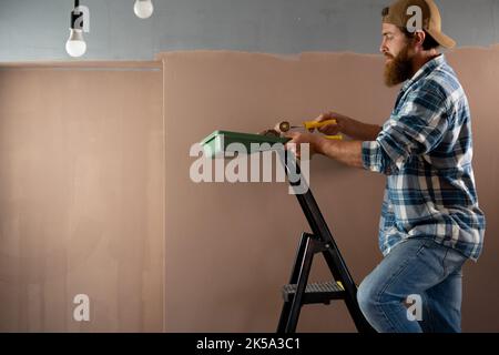 Maler malte eine Wand auf einer Leiter auf orangefarbenem Hintergrund Stockfoto