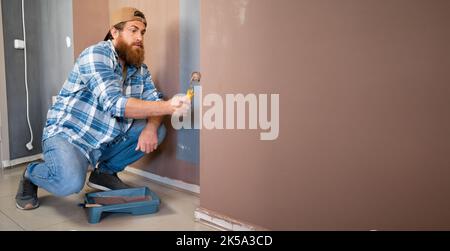 Zimmerlackierung. Kaukasischer bärtiger Zimmermaler mit Rollenmalerei. Stockfoto