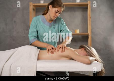 Schöne junge Frau, die eine Entspannungsmassage im Spa-Salon erhält. Professioneller Masseur macht therapeutische Massage zurück. Massagetherapie. Stockfoto