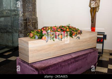 Sarg mit Blumen auf ihm in der Kirche mit Jezus Christus an der Wand warten auf den Transport für den Gottesdienst Stockfoto