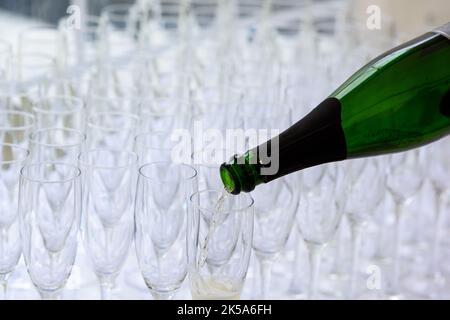 Nahaufnahme einer Champagnerflasche, die Champagner in eine Sektflöte vor einem verschwommenen Glas im Hintergrund pochelt Stockfoto