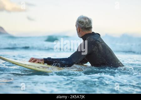 Wasser, Board und Surfer surfen die Wellen am Strand während des Urlaubs in Thailand während des Sonnenaufgangs im Sommer. Mann im Meer mit einem Surfbrett auf einer Reise Stockfoto