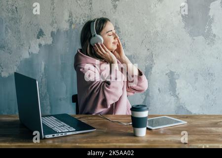 Eine Frau hört Musik über Kopfhörer, während sie eine Pause von der Fernarbeit auf einem Laptop hat. Stockfoto