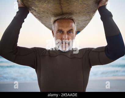 Strand, Surfbrett auf dem Kopf und ein reifer Surfer Mann mit Meereswellen und Meersand. Freiheit, Wassersport und Spaß im Seniorenurlaub in Australien Stockfoto