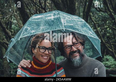 Beziehung und Liebe Paar unter dem Regen lächelnd und genießen Outdoor-Freizeitaktivitäten an regnerischen Tagen geschützt unter einem transparenten Regenschirm. Mann und Stockfoto