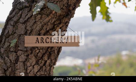 Bogenschießen auf Holzfläche geschrieben. Hintergrund Baumblätter. Gesundheit und Sport. Stockfoto