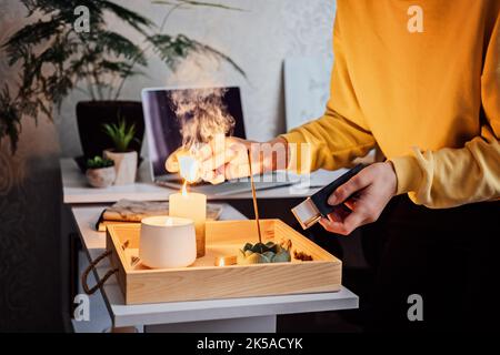 Meditation, Entspannung nach der Arbeit. Frau macht sich bereit, meditiert und zündet indischen Räucherstäbchen und Kerzen an. Frau Hände mit Rauch indian Stockfoto
