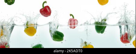 Viele bunte Paprika, die in Wasser spritzt. Seitenpanorama auf weißem Hintergrund. Stockfoto